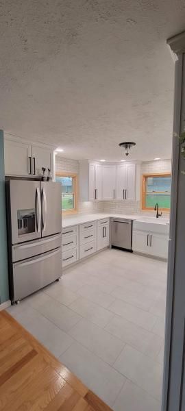 Bright white modern kitchen with stainless fridge, gray cabinets, tile floor, and window above the sink