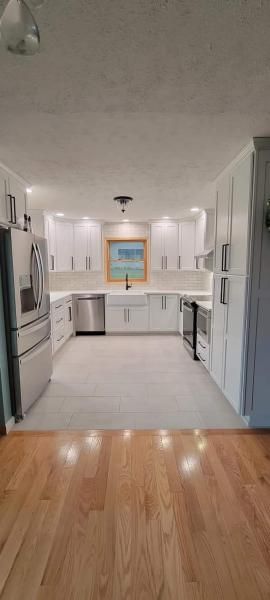 Bright open kitchen with white cabinets, tile floor, and hardwood in the foreground