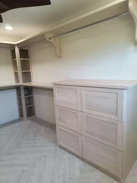 Empty built-in closet with light wood drawers, shelves, and hanging rod in a room with herringbone floor.