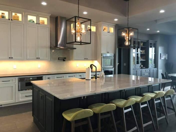 Modern kitchen with large island, green stools, white cabinets, and pendant lights
