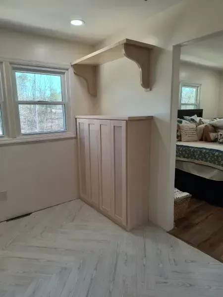 Built-in wardrobe cabinet under a shelf in a small bedroom with windows and herringbone wood floor