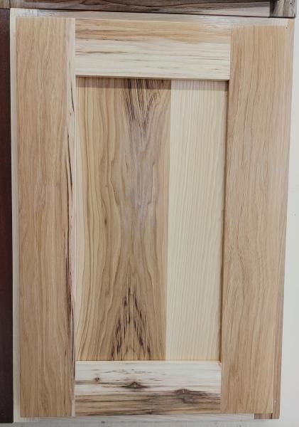Close-up of a light wood cabinet door with a framed, two-tone wood panel design
