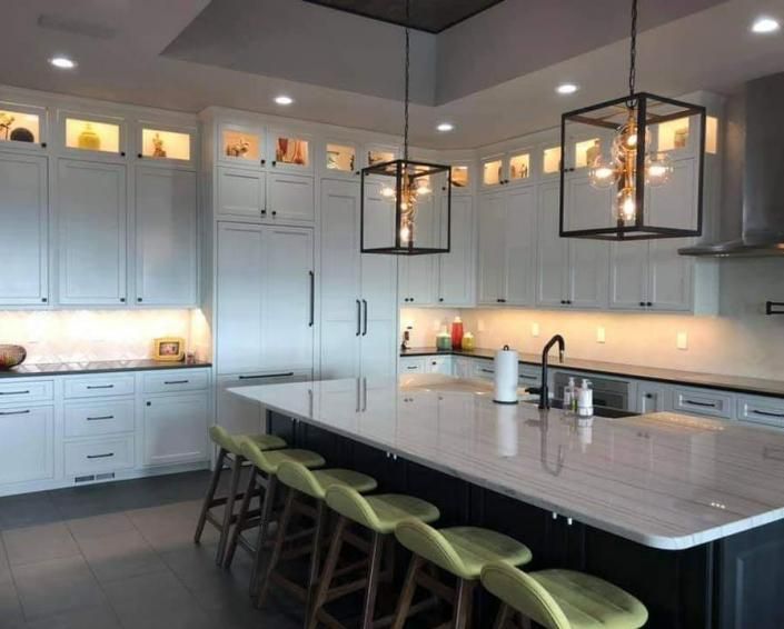 Modern kitchen with white cabinets, large island, green stools, and black pendant lights