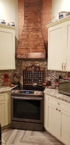 Kitchen with stainless stove and hood, white cabinets, and brick accent wall.