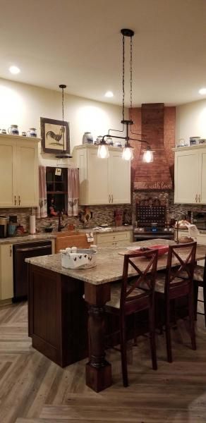 Warm kitchen with island, pendant lights, bar stools, cream cabinets, and brick backsplash