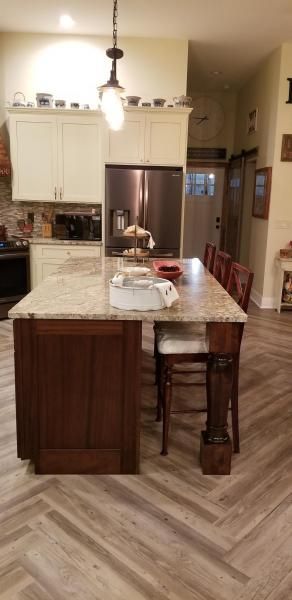 Kitchen with a large island, white cabinets, stainless fridge, and wood-look floor.