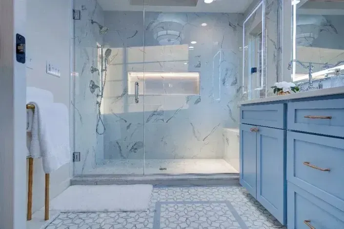 Modern marble bathroom with glass shower, blue vanity, and patterned tile floor