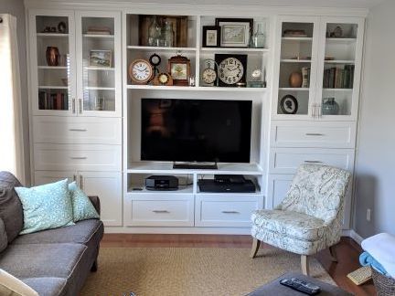 Living room with white built-in cabinets, a TV, and decorative shelves beside a gray sofa and patterned chair