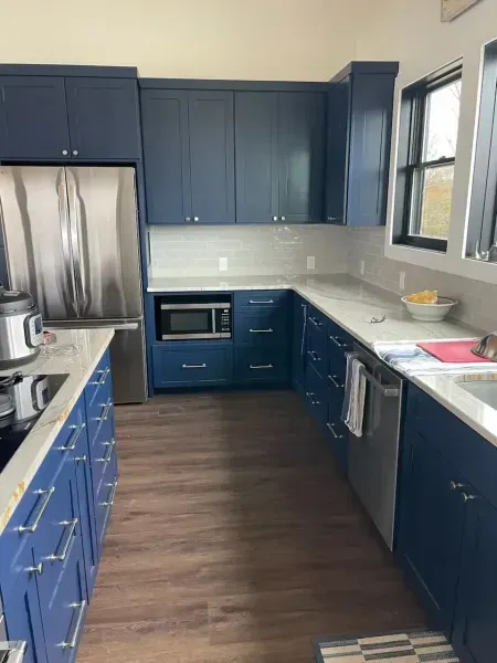 Blue kitchen with stainless steel appliances, white countertops, and wood flooring, viewed from the doorway