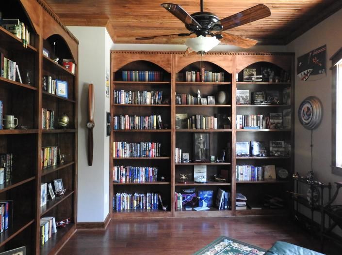 Wood-paneled living room with bookshelves, a ceiling fan, and a hardwood floor.