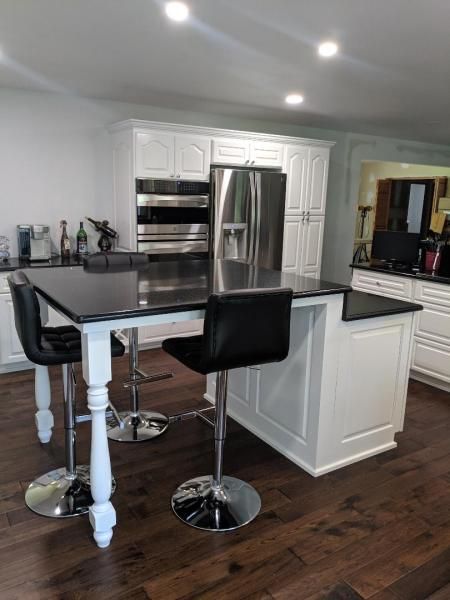 Modern kitchen with stainless steel appliances, white cabinets, and a dark island with two black stools.