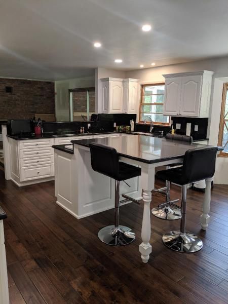 Modern kitchen with dark wood floors, white cabinets, black island stools, and stainless steel appliances