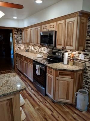 Narrow kitchen with wood cabinets, granite countertops, stainless stove, and mosaic tile backsplash.