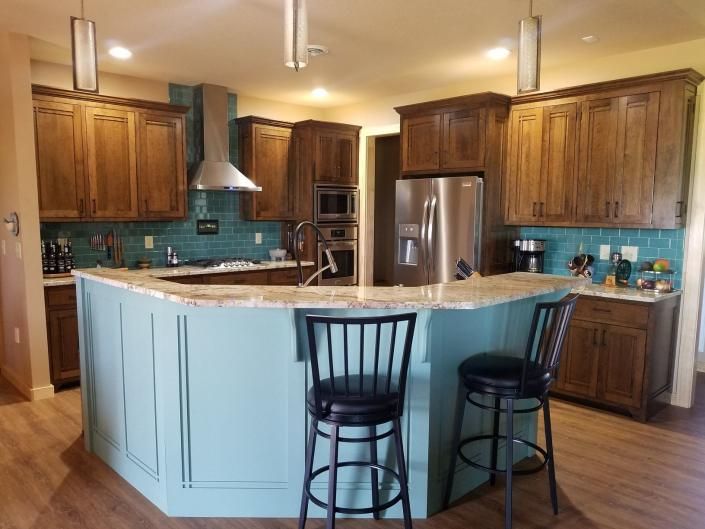 Bright kitchen with wood cabinets, granite island, and two black bar stools under warm lighting