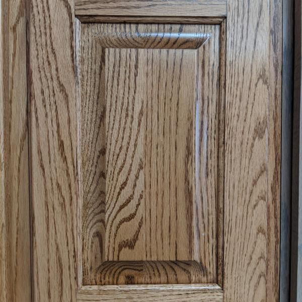Close-up of a light oak cabinet door with recessed paneling and brass hardware