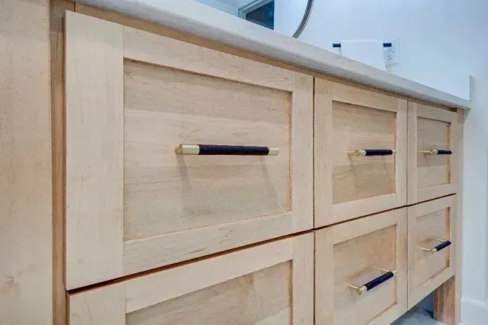 Light wood cabinet with six drawers and black-and-gold handles against a white wall