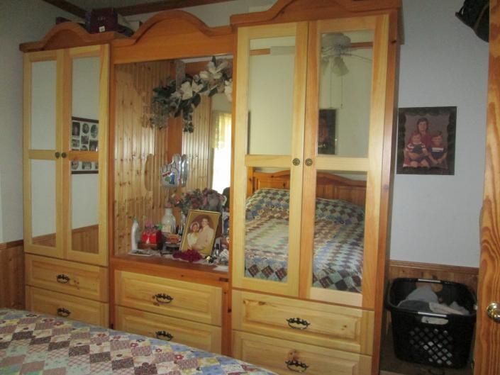 Wooden bedroom wardrobe with mirrored doors, dresser drawers, and a bed reflected in the center mirror.