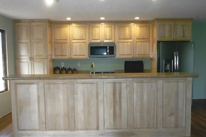 Spacious kitchen with light wood cabinets, a long island, recessed lights, and a refrigerator on the right.