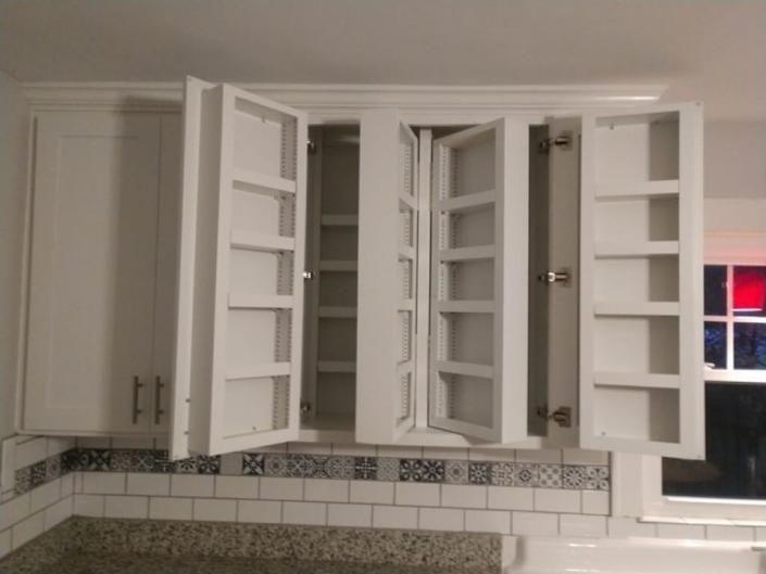 White kitchen cabinets with several open doors above a tiled backsplash and sink area