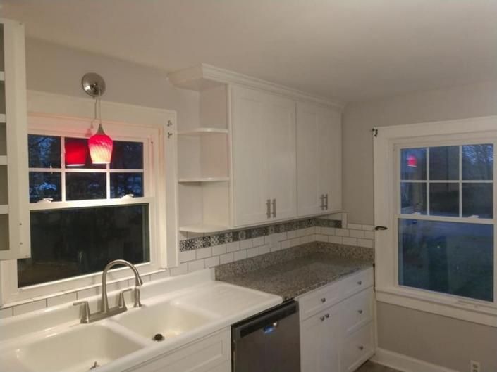 Bright white kitchen with sink, granite counters, red pendant light, and two windows at dusk