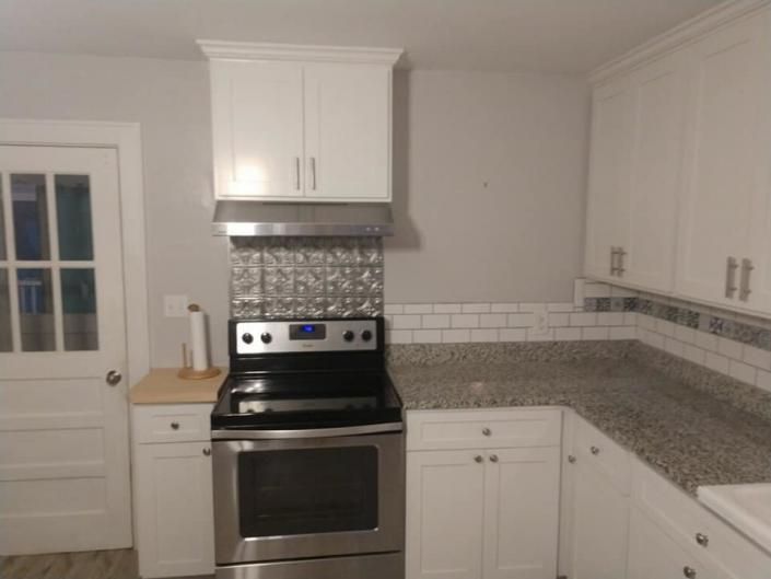 White kitchen with stainless steel stove, white cabinets, and gray countertop and backsplash.