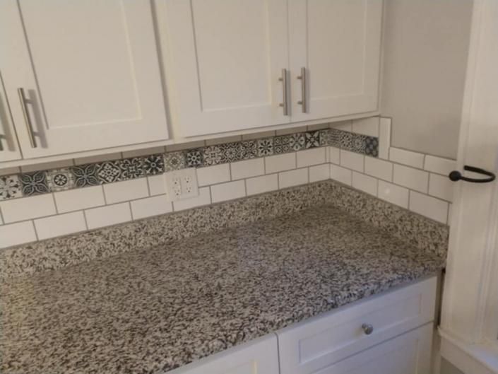 Granite kitchen countertop with white cabinets and decorative tile backsplash