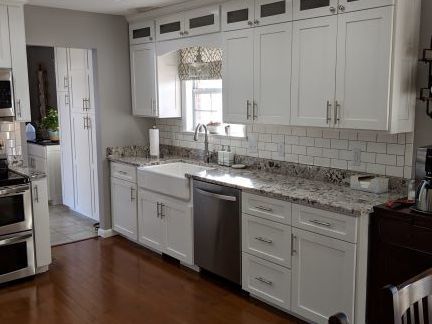 Bright white kitchen with cabinets, granite counters, stainless dishwasher, and hardwood floor.