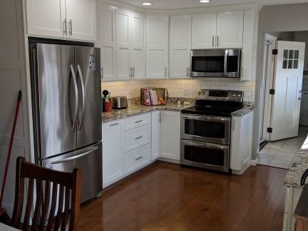 Modern kitchen with stainless steel fridge and stove, white cabinets, and hardwood floors