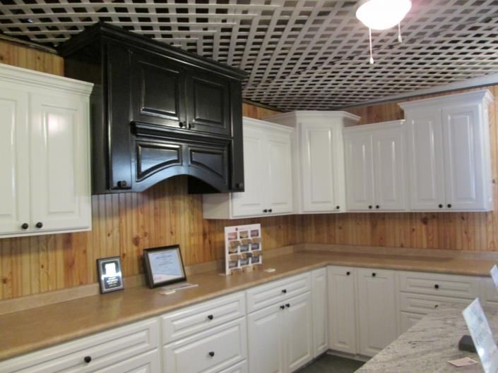 White kitchen with wood countertops, black range hood, and white cabinets against wood-paneled walls