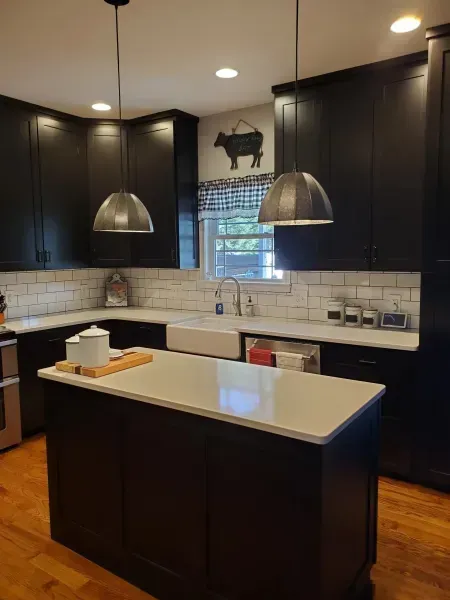 Modern kitchen with dark cabinets, white island, pendant lights, and hardwood floors