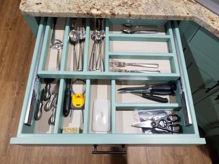 Open kitchen drawer with dividers holding utensils, knives, scissors, and a yellow tape measure