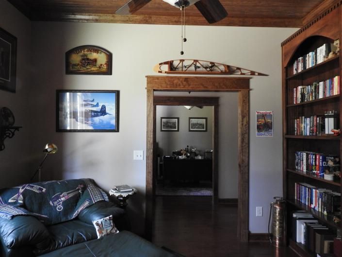Living room with dark sofa, doorway, bookshelf, and ceiling fan on a light beige wall