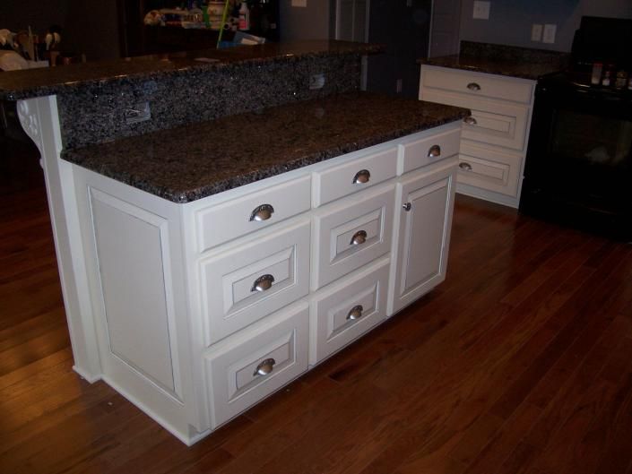 White kitchen island with granite countertop and drawers on a hardwood floor in a kitchen.