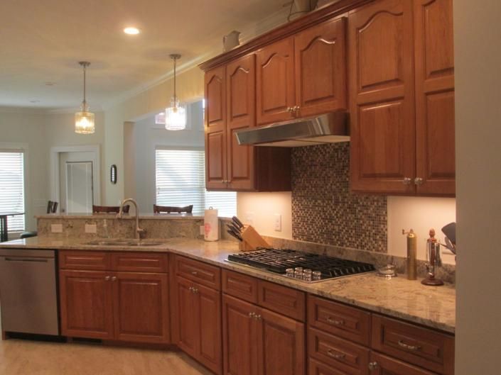 Bright kitchen with wooden cabinets, granite countertops, pendant lights, and a gas stove.