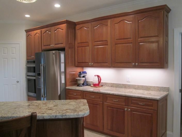 Kitchen with wooden cabinets, stainless fridge, beige countertops, and a granite island.