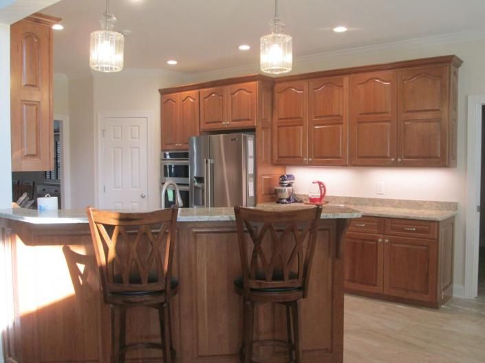 Modern kitchen with wood cabinets, stainless fridge, island, and two bar stools under pendant lights