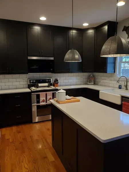 Modern kitchen with dark cabinets, white island countertop, pendant lights, and hardwood floors