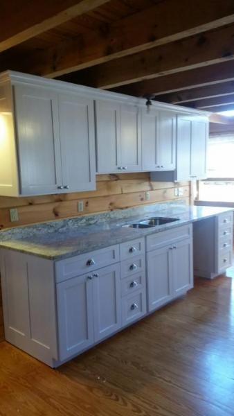 White kitchen cabinets and countertops in a rustic wood-paneled room with hardwood floors