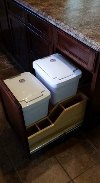 Two small lidded trash bins, beige and white, in a pull-out cabinet under a kitchen counter.