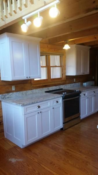 Rustic kitchen with white cabinets, black stove, wood ceiling, and hardwood floor