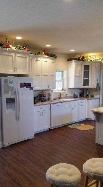 Bright kitchen with white cabinets, white fridge, wood floor, and a small cushioned stool in the foreground