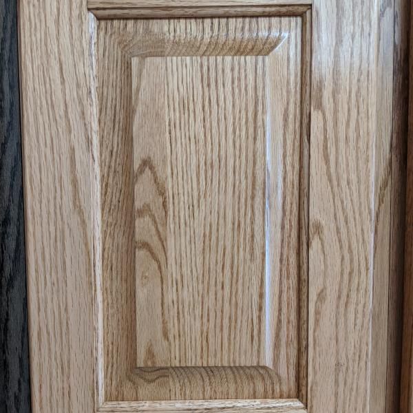 Close-up of a wooden cabinet door with raised paneling and oak grain.