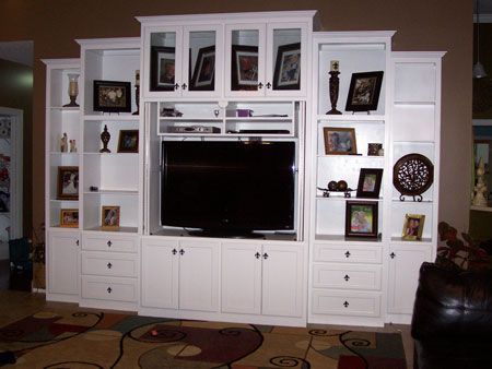 White entertainment center with TV, shelves, drawers, and framed photos in a living room