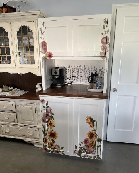 White cabinet with floral sunflower decals in a kitchen corner next to a counter and open door