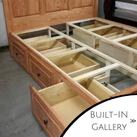 Wooden built-in bed frame with open storage drawers pulled out in a bedroom.