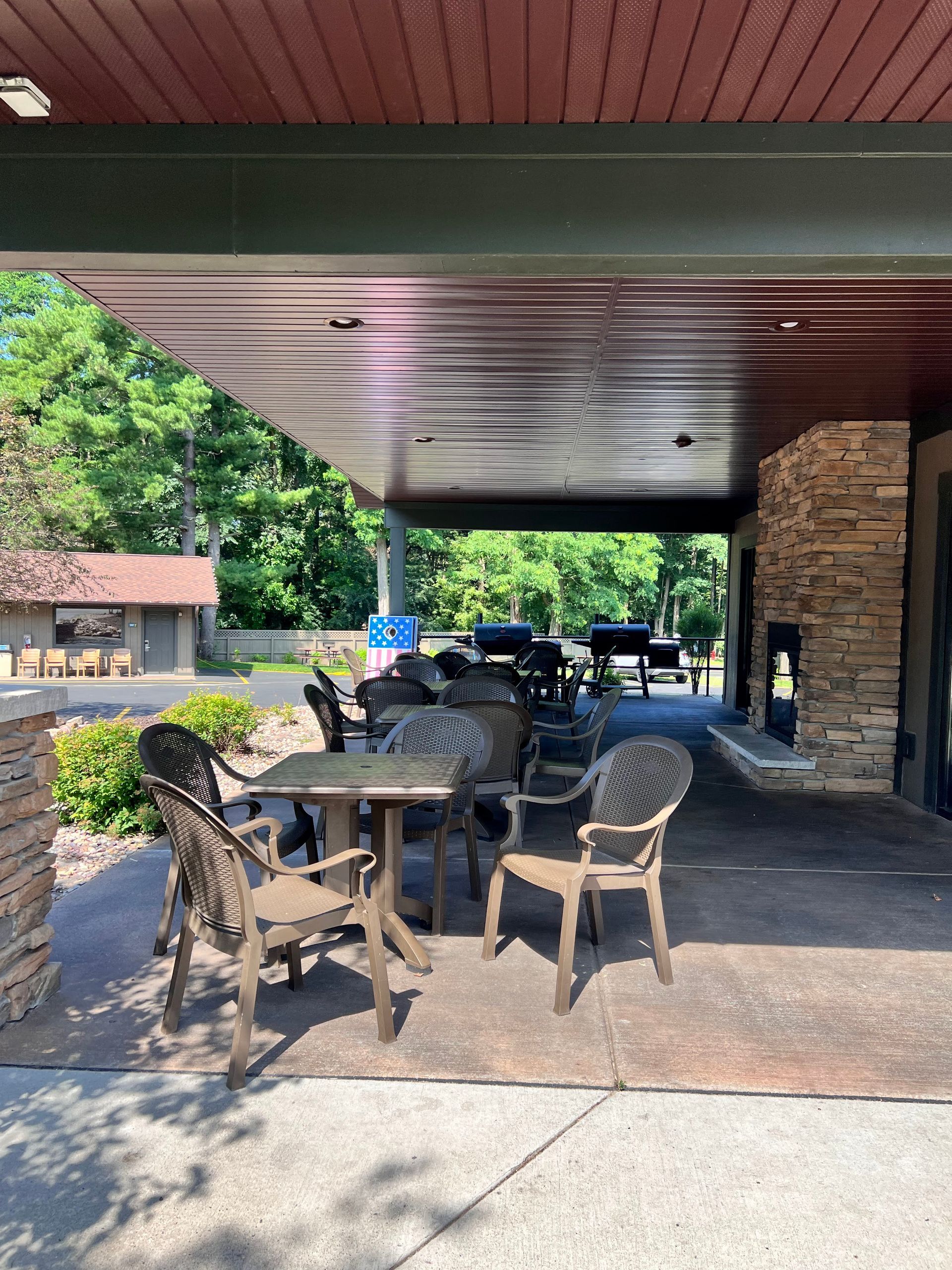 Covered outdoor patio with wicker chairs, tables, and parked golf carts beside a stone building.