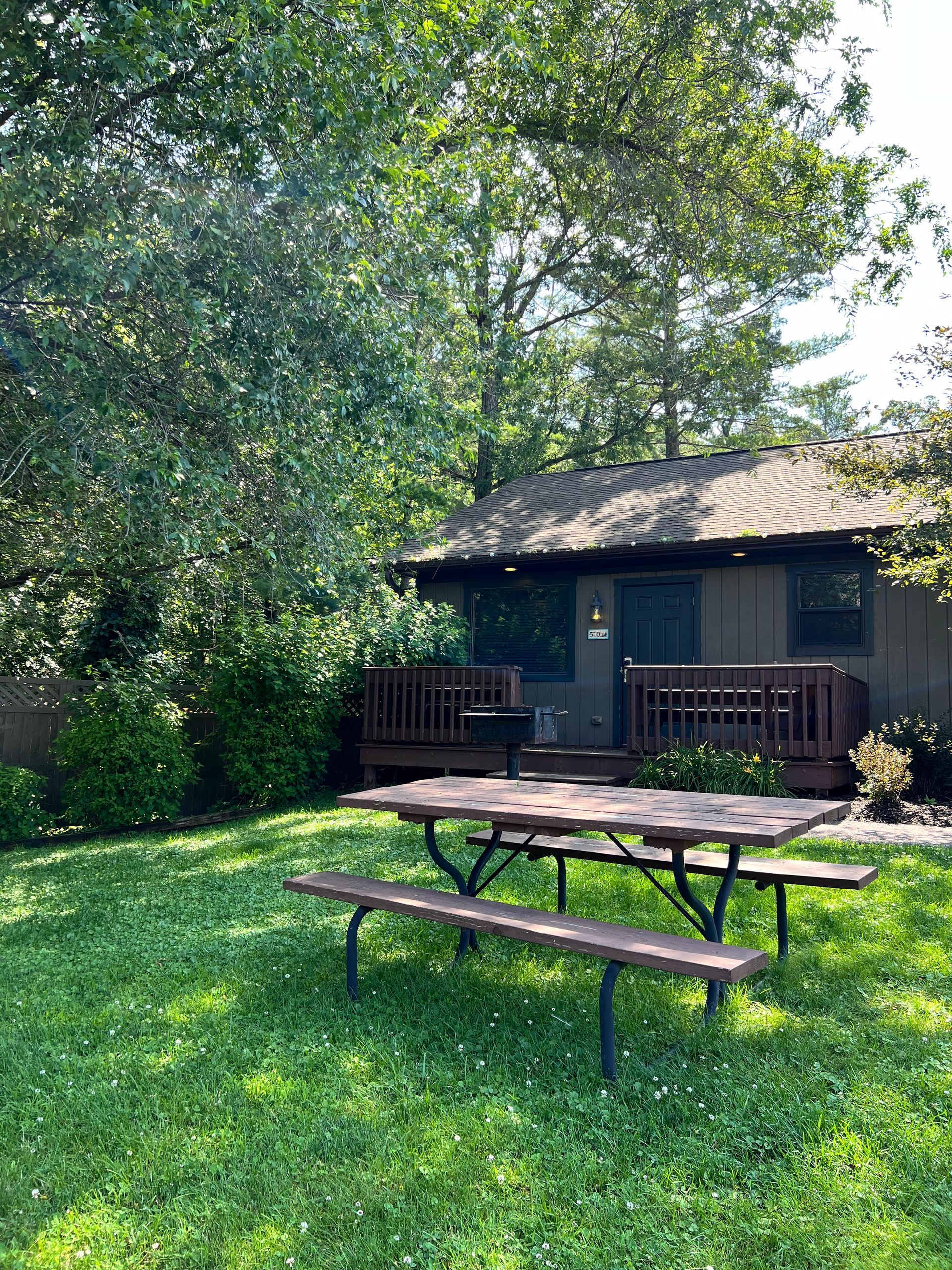 Grassy yard with a picnic table in front of a small cabin under trees
