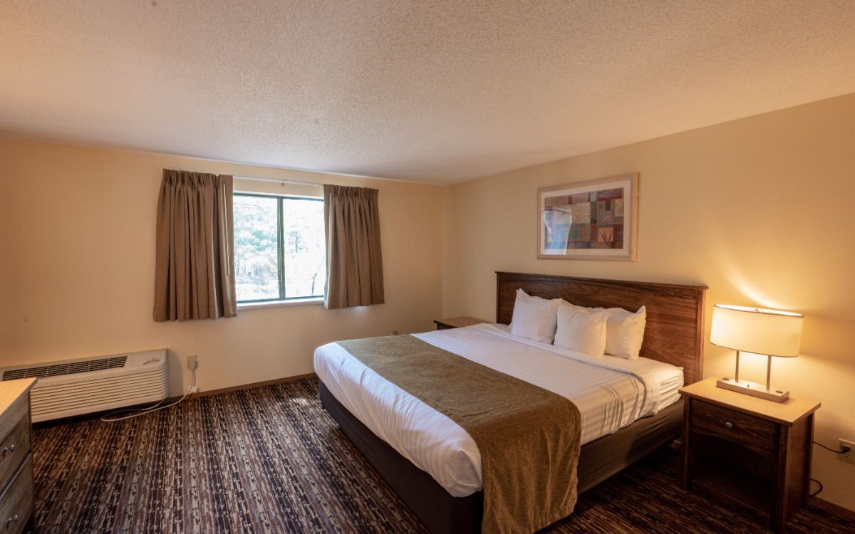 Cozy bedroom with a large bed, bedside lamp, window with curtains, and patterned carpet.