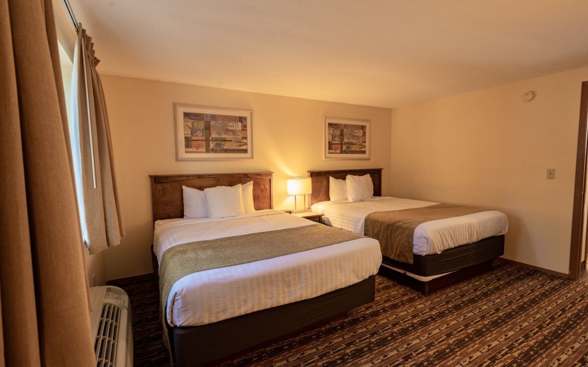 Hotel room with two neatly made beds, bedside lamp, and beige walls