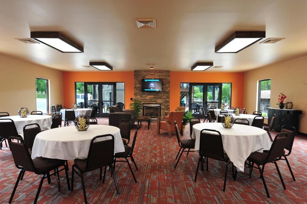 Empty banquet room with round tables, black chairs, red carpet, and orange walls in a bright dining hall